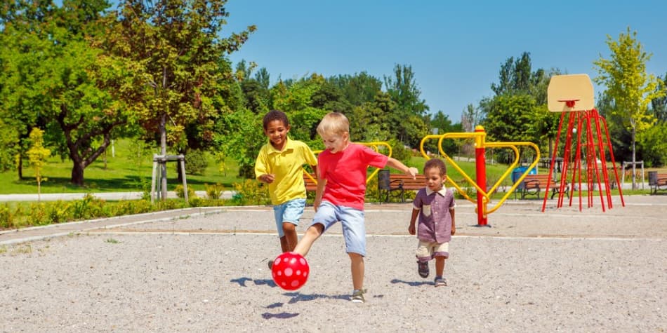 Three young children kicking a ball on a playground